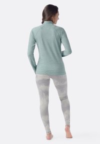 Long-sleeve, light teal athletic shirt with a high collar, paired with patterned, light gray leggings featuring a subtle abstract design.