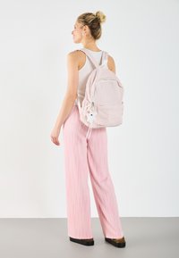 Light pink checkered backpack with drawstrings and a small white character charm. Paired with pink striped wide-leg pants and a white top.