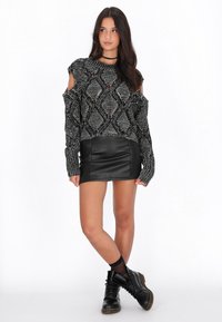 Maglione lavorato a maglia in bianco e nero con spalle scoperte abbinato a una minigonna in pelle sintetica nera e stivali neri con lacci.