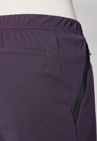 Lila tygträningsshorts med elastiskt midjeband, en sidoficka med dragkedja och texturerad detalj på materialet.