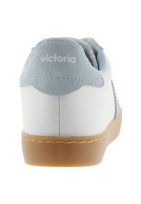 Baskets blanches avec un tirant en suède bleu clair et une semelle en gomme, vues de l'arrière, montrant les coutures et le nom de la marque sur le tirant.