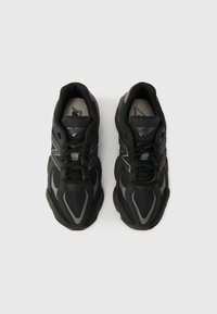 Black athletic shoes featuring a mesh and synthetic upper, rounded toe, thick rubber sole, and reflective detailing on the sides.
