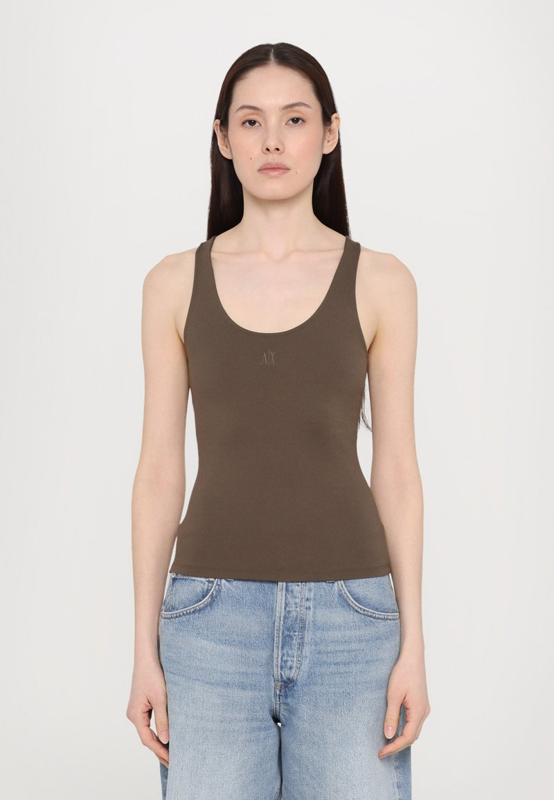 Top in cotone marrone con scollatura a forma di barca e spalline larghe, realizzato in tessuto liscio. Presenta un piccolo logo al centro. Indossato con jeans azzurri chiari.
