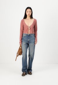 Röd rutigt kort topp med långa ärmar och knytning, parat med högmidjade blåjeans, brun handväska och skor med djurmönster.