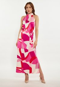 Rochie maxi colorată, fără mâneci, cu un guler înalt, având modele abstracte roz și roșu pe un fundal crem și o talie evidențiată cu un cureaua.