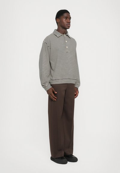 Polo rayé à manches longues en beige et noir, en coton, avec un col et une patte de boutonnage à trois boutons. Assorti à un pantalon ample marron.