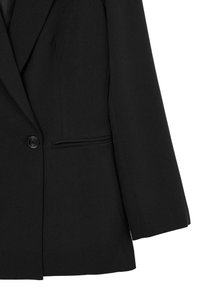 Blazer nero con rever a punta, chiusura a un bottone e una vestibilità snella e su misura con una texture liscia.