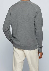 Felpa grigia con scollatura a girocollo, maniche lunghe a raglan e orlo a costine. Presenta un tessuto testurizzato e un design minimalista, senza loghi visibili.