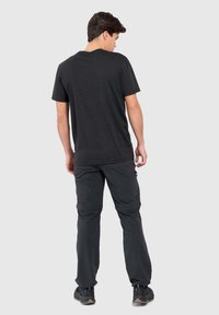 Zwarte korte mouwen t-shirt gecombineerd met donkere cargo-broeken. De outfit heeft een ontspannen pasvorm en een zachte textuur. Zichtbare stiksels en zakken.