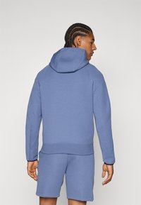 Felpa con cappuccio blu dal finish testurizzato, con cappuccio regolabile tramite cordino e polsini elasticizzati, abbinata a pantaloni corti coordinati.