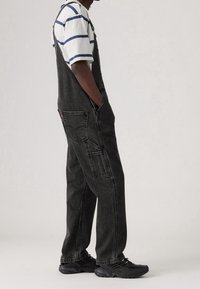 Svarta denimoveraller med en avslappnad passform och fickor, para ihop med en randig kortärmad skjorta och svarta sneakers.