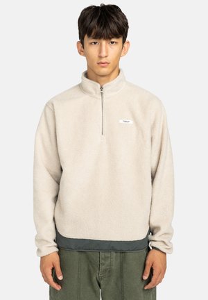 Fleece pullover in licht beige met een halve ritssluiting, hoge kraag en contrasterende donkergroene zoom. Bevat een klein logo op de borst.