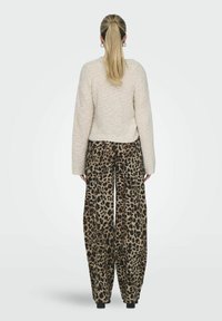 Pullover di maglia con texture cremosa e vestibilità ampia, abbinato a pantaloni a gamba larga con stampa leopardata e vita alta. Dei blocchi neri enfatizzano l'outfit.