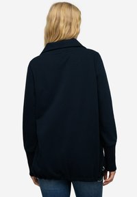 Maglione blu navy con un ampio colletto, dettagli in costa sui polsini e orlo elastico. Tessuto morbido con una vestibilità rilassata, mostrato da dietro.