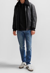 Svart läderbomberjacka med pälskrage, dragkedja och ribbade mudd, kombinerad med blå jeans och vita sneakers.