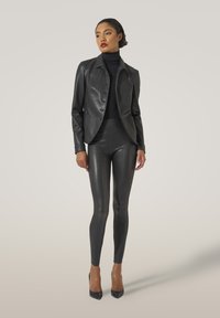 Svart fusk läderjacka med spetsig krage, knappstängning, i kombination med glänsande svarta leggings. Klackar med en beige accent.