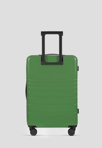Groene harde koffer met geribbelde textuur, zwarte telescopische handgreep en vier wielen voor mobiliteit. Compact en rechthoekig ontwerp.