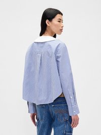 Pruhovaná košile s dlouhým rukávem v modré a bílé barvě s bílým límcem, s volným střihem a plisovaným detailem na zadní straně. Knoflíky na rukávech.