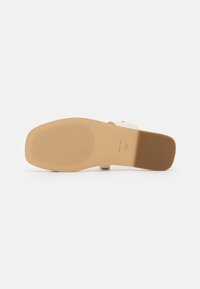 Semelle plate de sandale avec avant en caoutchouc beige texturé et talon marron lisse, taille 7,5M, vue par le dessous sur fond blanc.