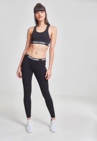 Crna sportska crop majica i uske tajice u skladu s logom "URBAN CLASSICS" na pojasu. Napravljen od rastezljivog materijala; prilagođen dizajn. Bele patike.