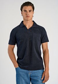 Donkerblauw poloshirt van zachte stof, met een ovale kraag, korte mouwen en een borstzak. Draag het met blauwe jeans.