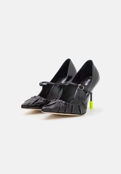 Black leather high-heeled shoes with a pointed toe, textured finish, ankle strap, and a distinctive neon green heel accent.