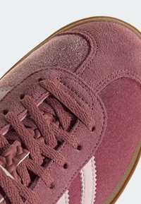 Růžové tenisky kombinující semišové a hladké materiály, s texturovanými tkaničkami, výraznými bílými proužky a gumovou podrážkou.