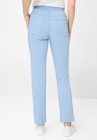 Lichtblauwe stretchbroek met een aansluitende tailleband, recht gesneden ontwerp, twee achterzakken en subtiele stikdetails. Gedragen met witte sneakers.