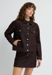 Giacca in denim marrone con colletto, due tasche frontali, bottoni dorati e design corto, abbinata a una gonna coordinata.