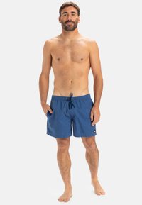 Modré plavkové šortky s textúrovanou tkaninou, elastickým pásom a nastaviteľnou šnúrkou. Obsahuje malé logo na dolnej strane.