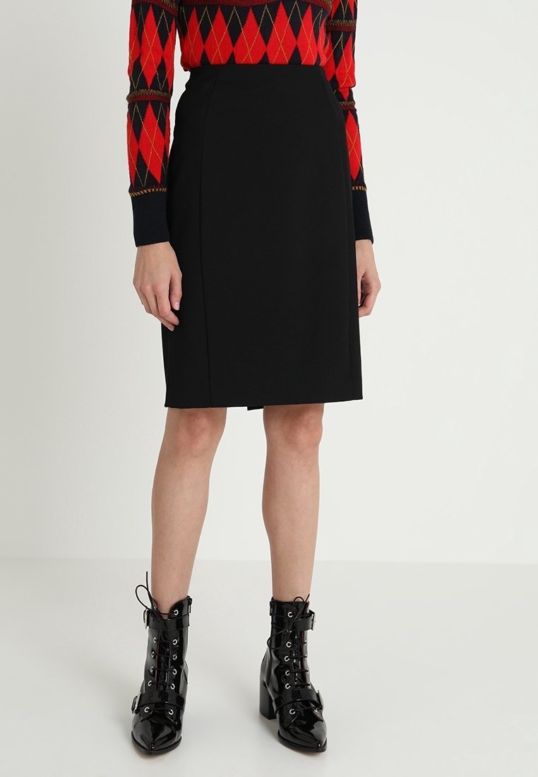 Femme portant une jupe crayon noire longueur genou, un pull en argyle rouge et noir, et des bottines à lacets en cuir verni noir.