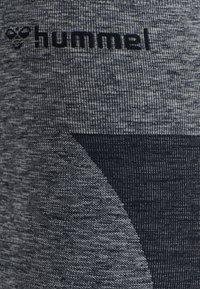 Gråtonade träningstights i ett strukturerat stickat material, med en kontrasterande mörk fläck och "hummel"-loggan nära midjan.