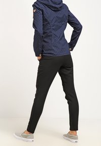 Marinblå vattentät jacka med vita prickar, huva och knappdetaljer, kombinerat med svarta slim-fit byxor och gråa slip-on skor.