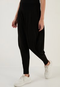 Zwarte harempants met geplooide details, gemaakt van zachte stof en taps toelopende benen. Gecombineerd met witte sneakers.