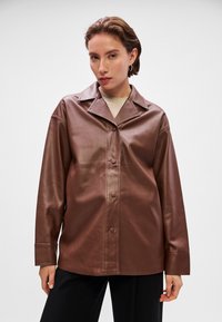 Casaco de pele sintética castanha com gola, fecho de botão e mangas longas. Textura suave e corte descontraído.