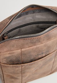 Braune Lederhandtasche mit einem Reißverschluss oben, ausgestattet mit einem gestreiften Innenfutter und einer Außentasche. Glatte Textur mit sichtbaren Nähten.