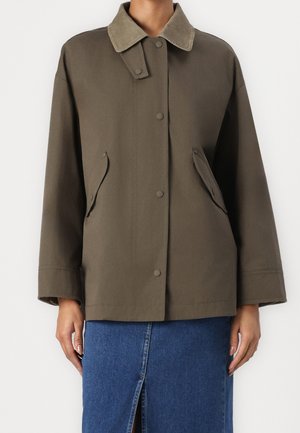 Olive green jacket with snap buttons, flap pockets, and a contrasting corduroy collar worn with a blue denim skirt featuring a front slit.