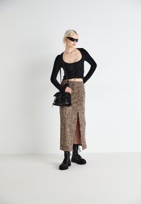 Haut noir à manches longues en tissu texturé, associé à une jupe midi imprimé léopard avec une fente à l'avant. Bottines noires et sac à main.