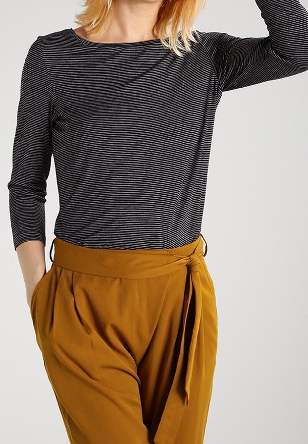 Schwarz-weißer gestreifter Langarmshirt kombiniert mit hoch taillierten, senfgelben Hosen, die eine gebundene Taille und eine plissierte Vorderseite haben.