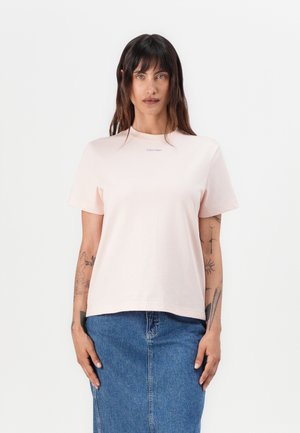 Light pink short-sleeve t-shirt made of cotton, featuring a round neckline and a small Calvin Klein logo on the front, paired with a denim skirt.
