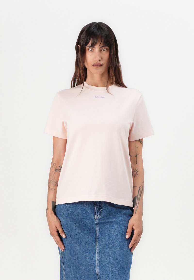 Lys rosa t-skjorte med korte ermer laget av bomull, med rund hals og en liten Calvin Klein-logo på forsiden, kombinert med et denim skjørt.