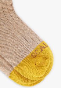Calcetines de color beige con textura acanalada y punteras en un brillante color amarillo, que presentan texto marrón parcial tejido en la zona de los dedos sobre un fondo blanco.