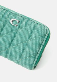 Green quilted wallet made of denim fabric, featuring silver hardware. The design includes a diamond pattern and a zip closure.