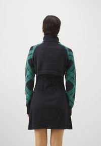 Pletena obleka z visokim ovratnikom, dolge rokave iz teal vzorčaste tkanine in oprijet bodice v črni barvi, ki se na robu razširi.