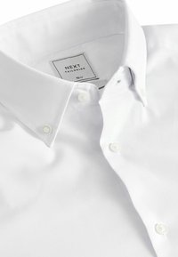 Biała koszula z długim rękawem, wykonana z teksturowanej tkaniny, z kołnierzykiem zapinanym na guziki i białymi guzikami. Metka mówi "NEXT TAILORING" w rozmiarze 15½.