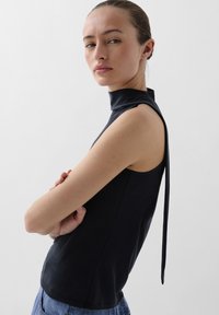 Zwarte mouwloze top met hoge nek en een strikdetail op de rug, met een gladde textuur en een getailleerd silhouet.