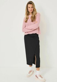 Helles rosa, flauschiges Sweatshirt, lockere Passform; schwarze Wickelrock bis zum Knie mit seitlichem Schlitz; weiße und beigefarbene Sneakers mit roten Akzenten und gepolsterten Zungen.