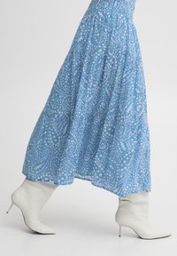 Rochie maxi cu un model albastru, având un design paisley, asociată cu cizme albe, ajustate, până la genunchi, cu vârf ascuțit și toc stiletto.
