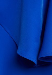 Tkanina w kolorze królewskim niebieskim z gładką teksturą; cechuje się miękkimi krawędziami i precyzyjnym ściegem, podkreślając płynny design odzieży.