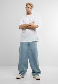 Hvid bomulds T-shirt med korte ærmer, parret med lyseblå oversized denim jeans. Hvide sneakers med røde accenter fuldender outfittet.